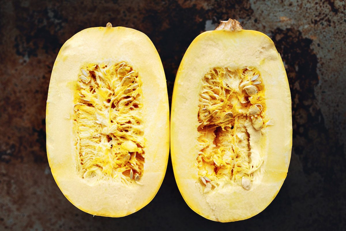 A halved raw spaghetti squash on a well seasoned baking sheet.