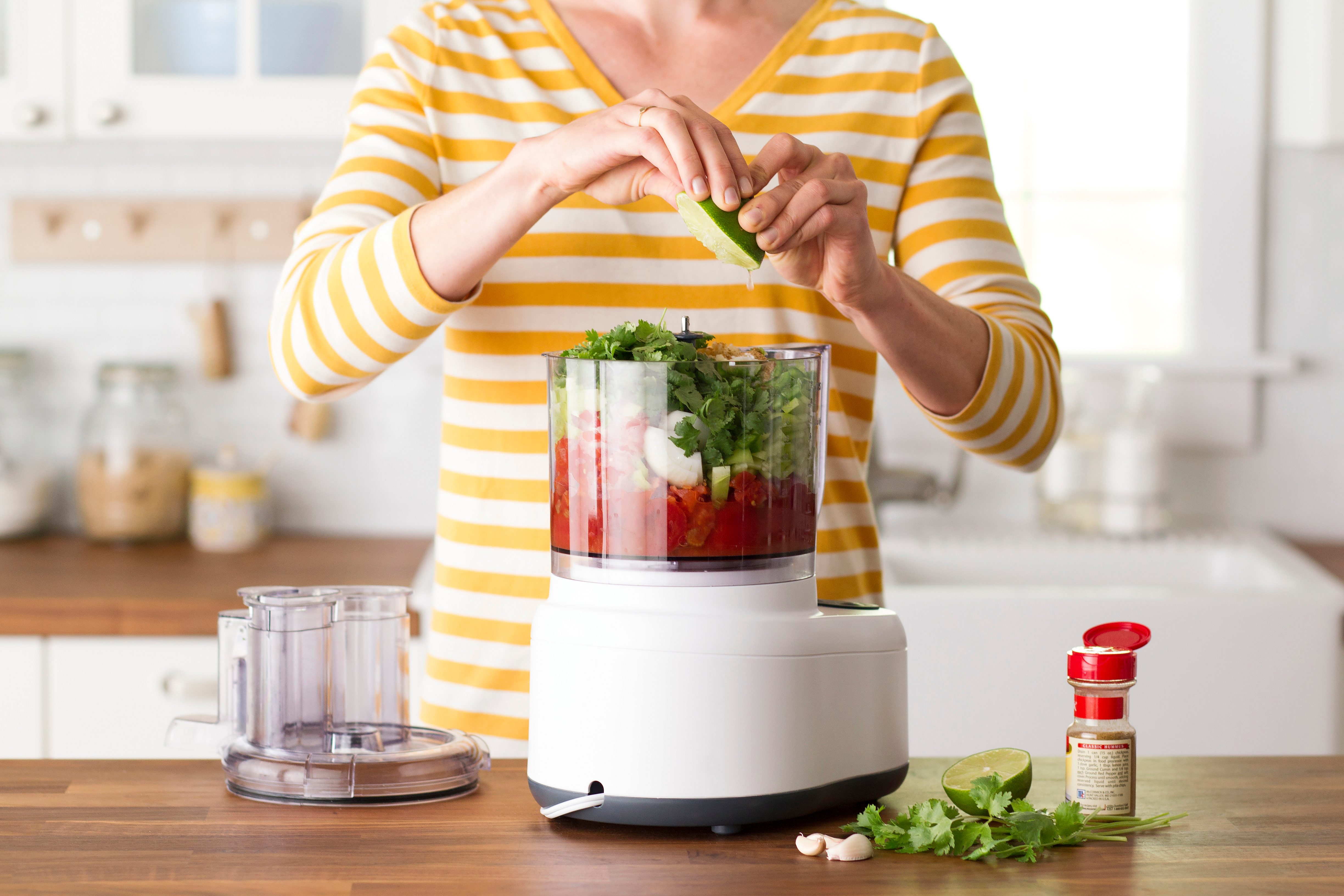 Person squeezing a lime over the salsa ingredients in their blender
