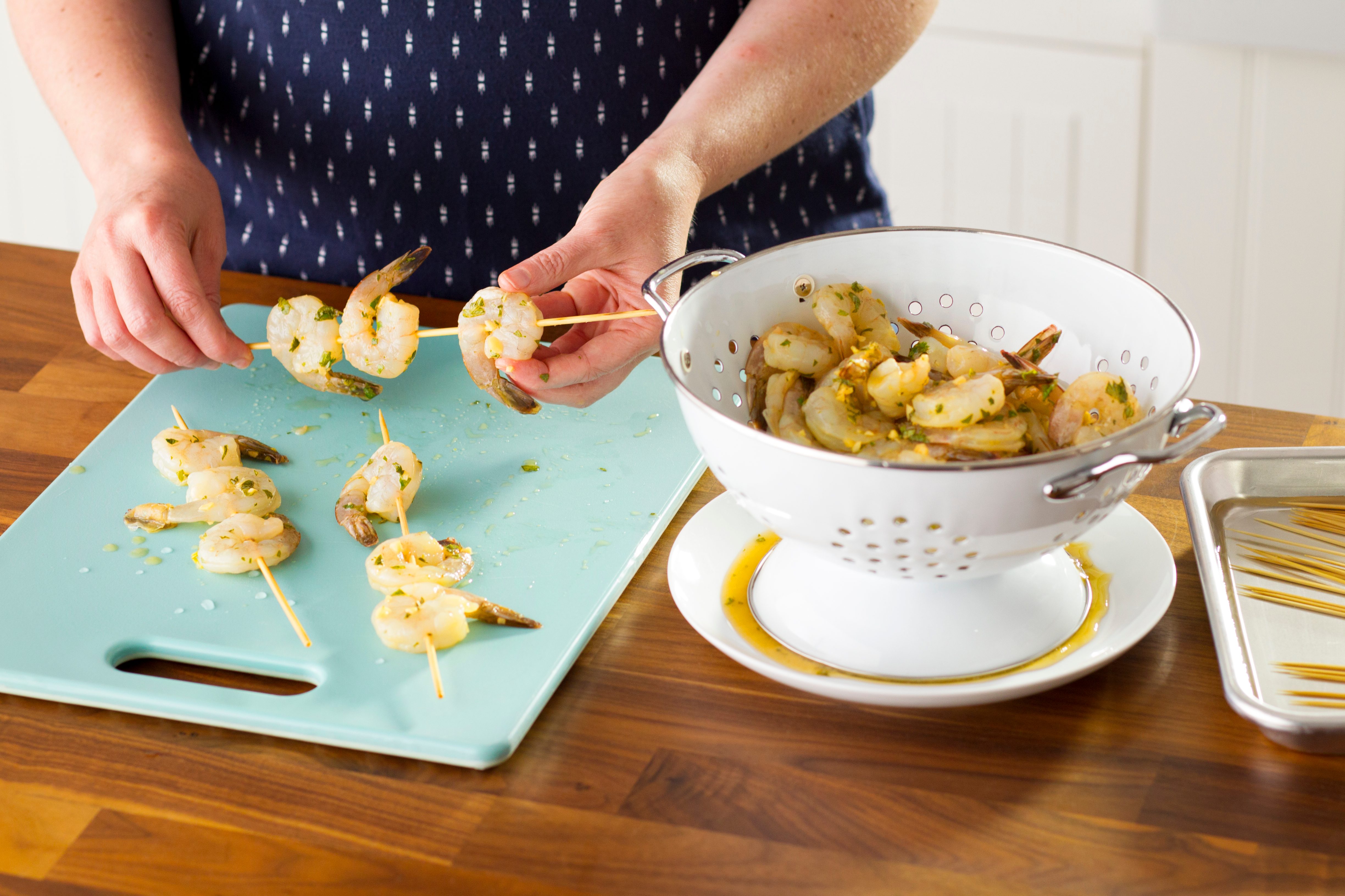 Person putting shrimp onto wooden skewers