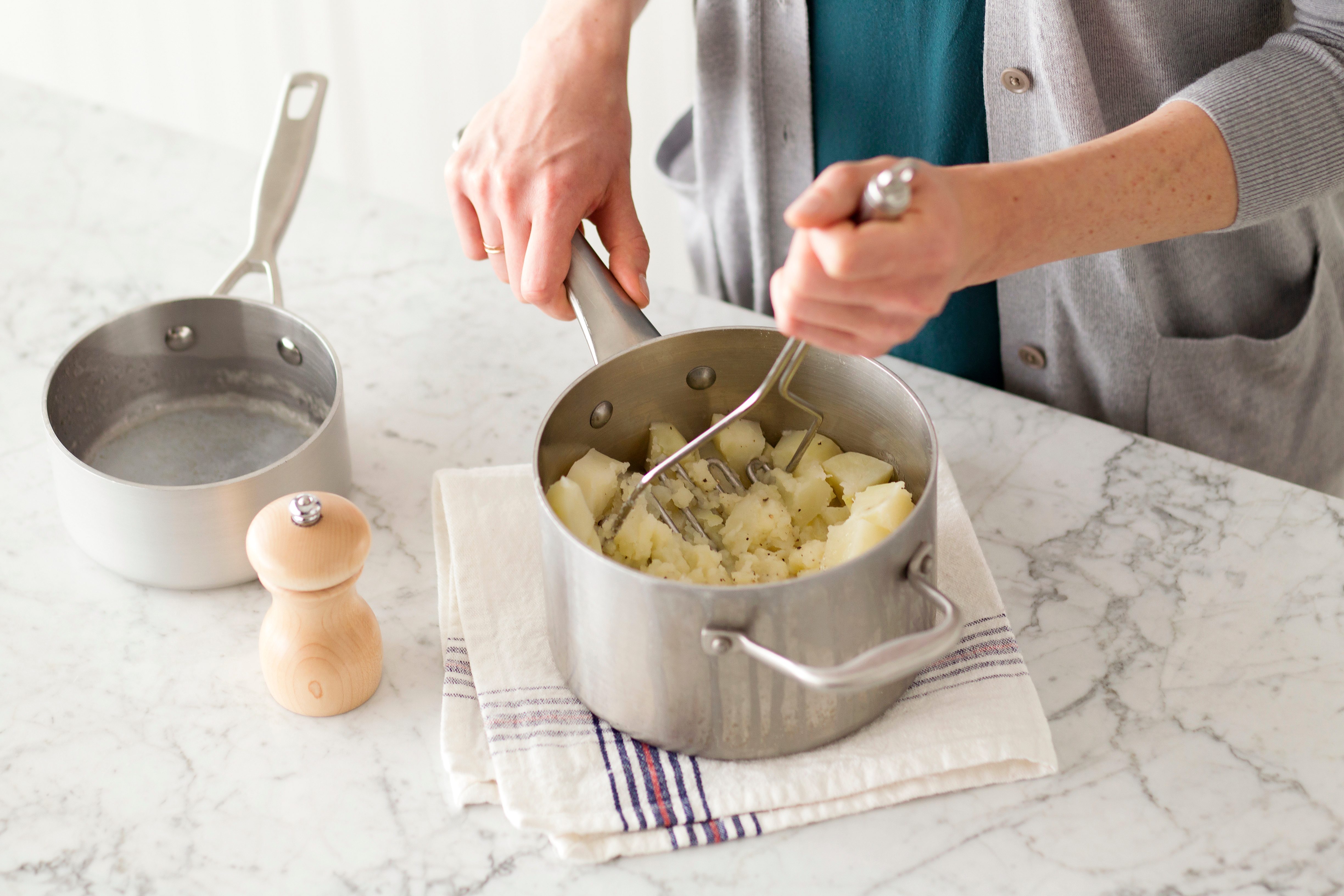 Person mashing potatoes in a metal pot