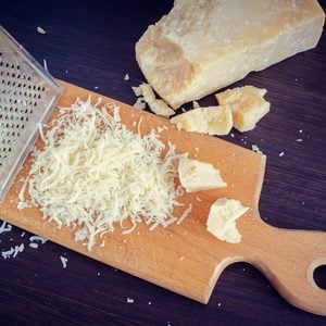 Heap of grated Parmesan cheese and metal grater on wooden board.