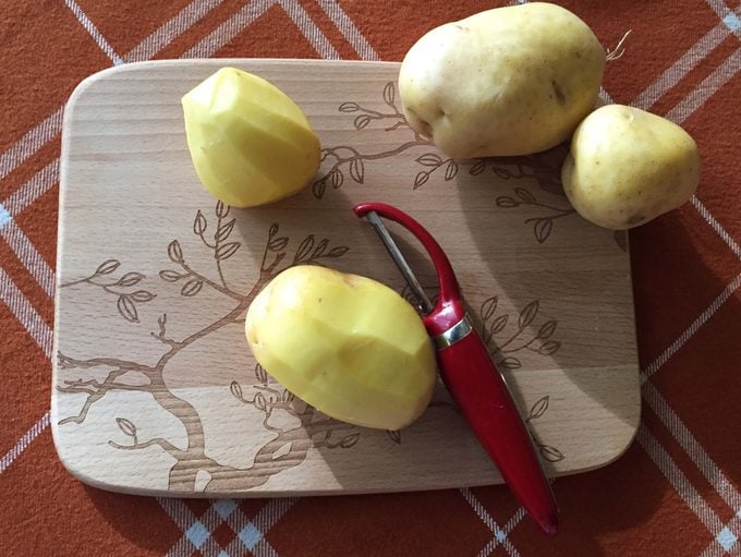 Potatoes being peeled on a wooden cutting board