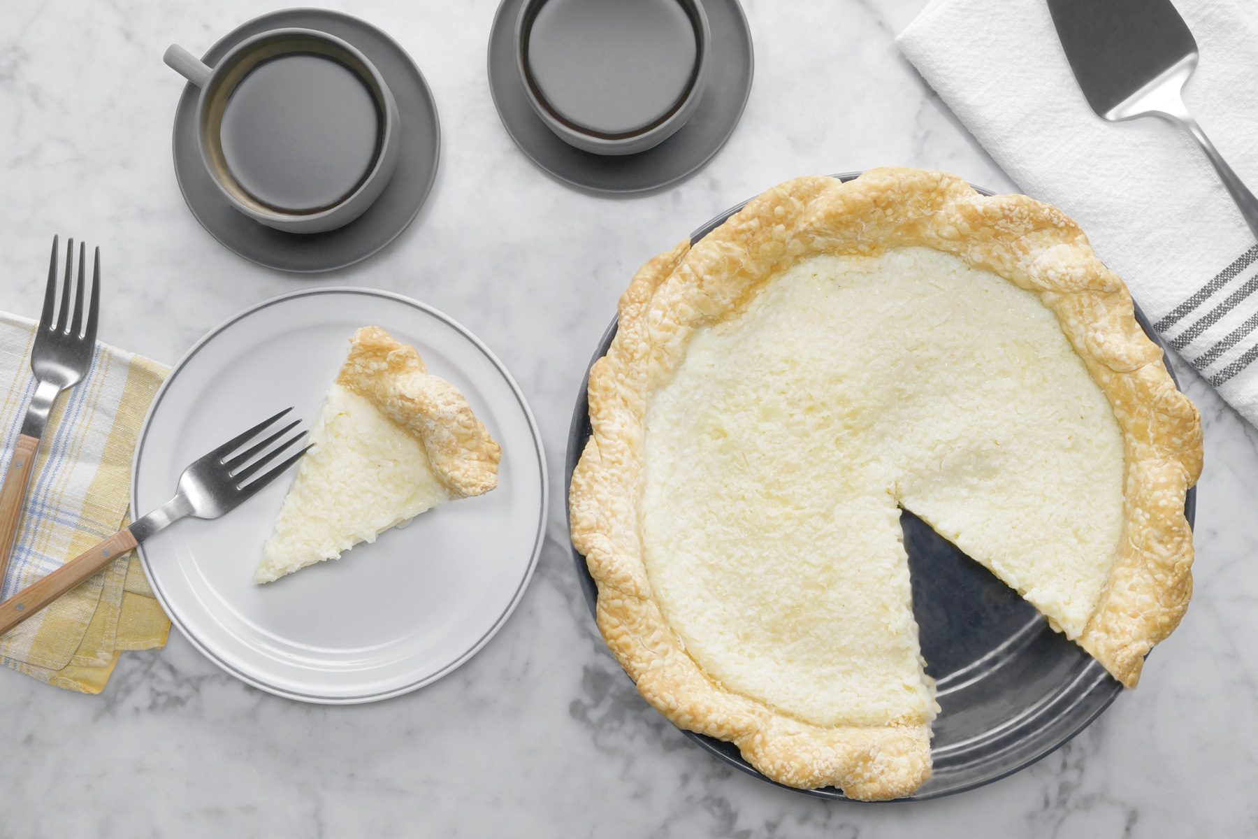 A coconut pie on a plate next to a fork and cups