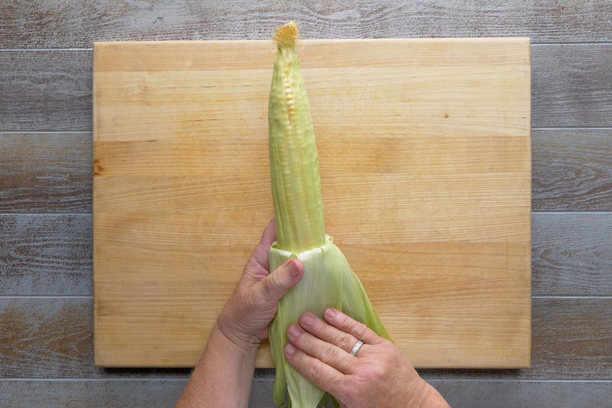 Peeling back husks of corn over wooden board