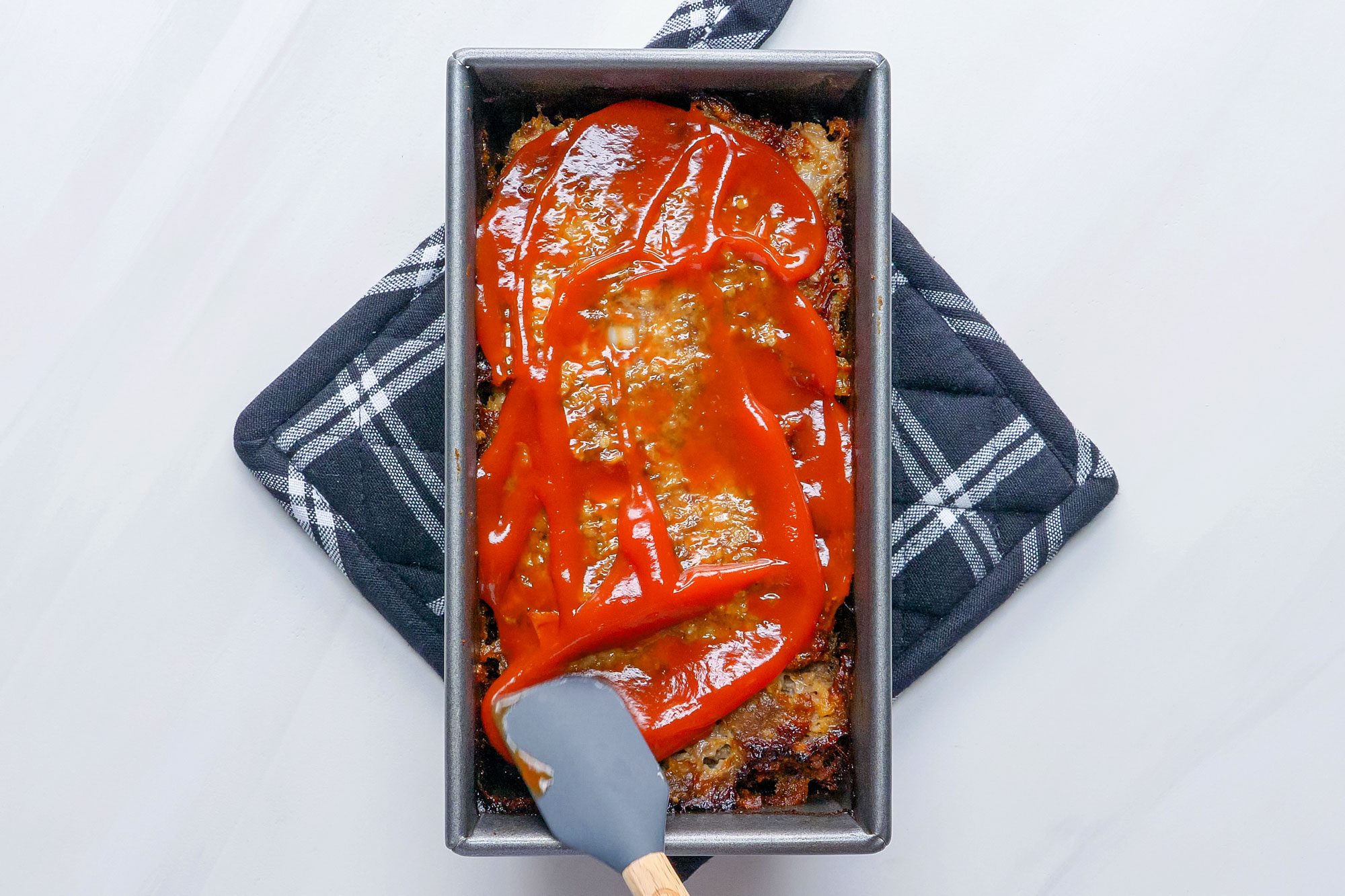 Spreading the ketchup over the meat loaf with spatula