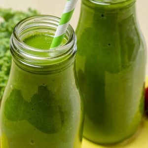Close up of healthy green juice smoothie in glass bottle sitting on yellow napkin with fresh strawberries and kale