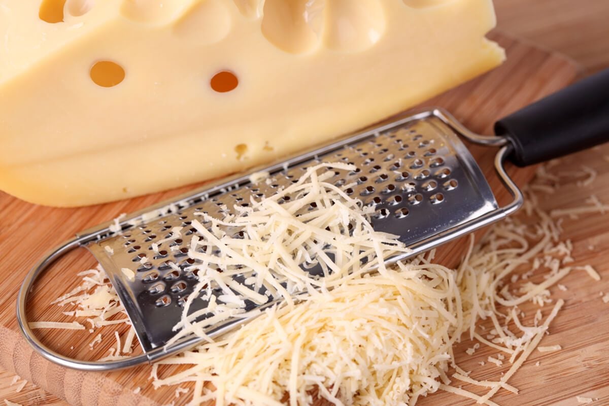 Grated cheese and grater on a wooden cutting board.