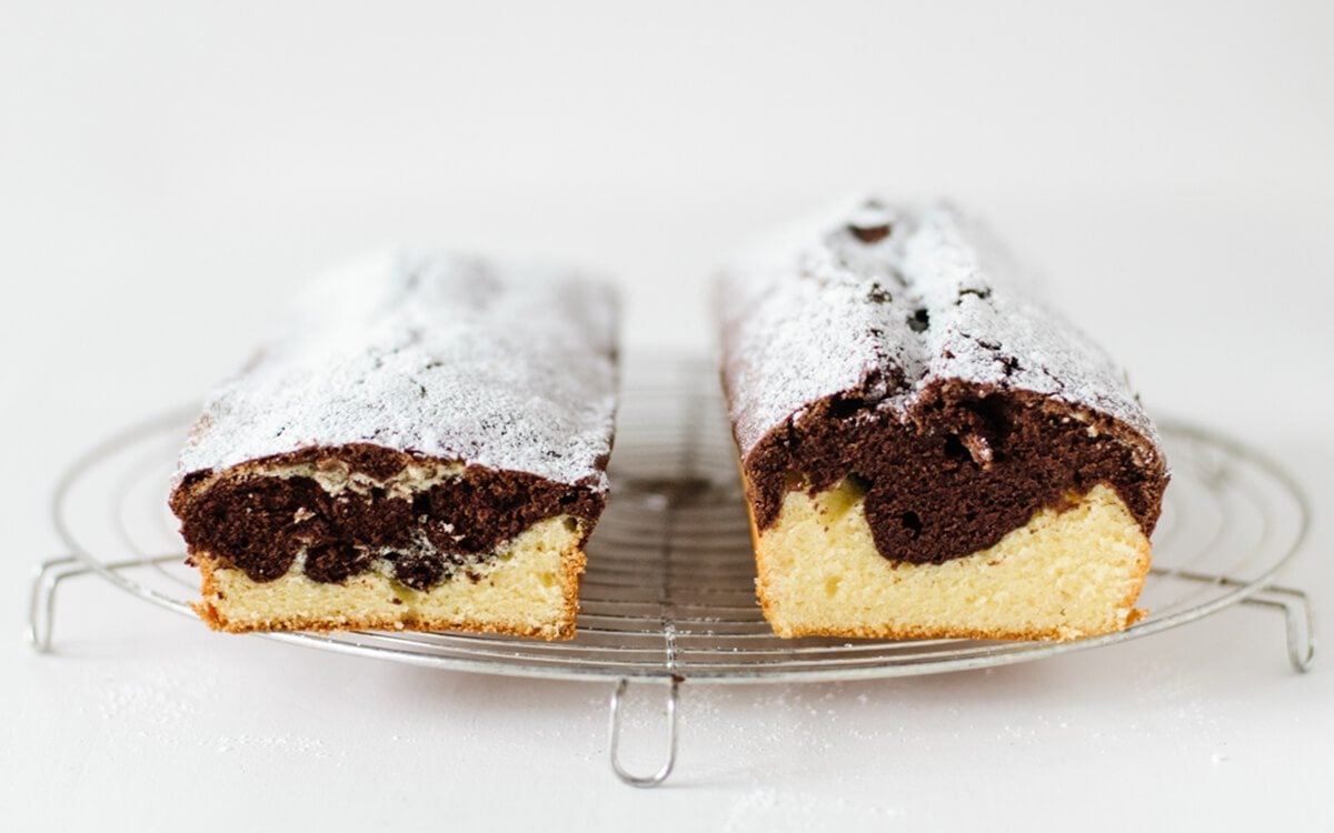Two different vanilla chocolate marble cakes dusted with powdered sugar next two each other for comparison to see baking mistakes or fails on cooling rack on white background