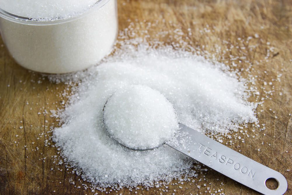 granulated sugar in spoon and sugar pile on wooden