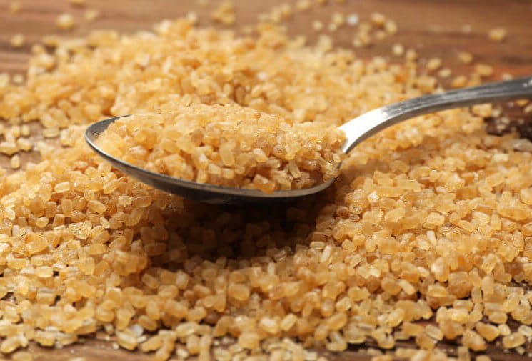 Heap of brown sugar and spoon on wooden background