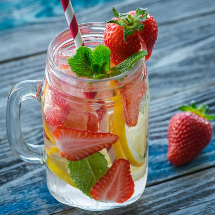 Jug with lemon and strawberry infused water on a rustic wooden table