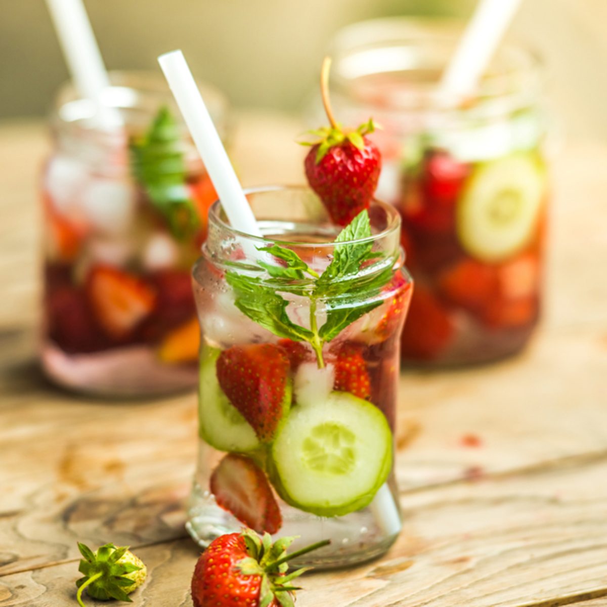 Three retro glass jars of lemonade with strawberries, cucumber and mint on wooden table