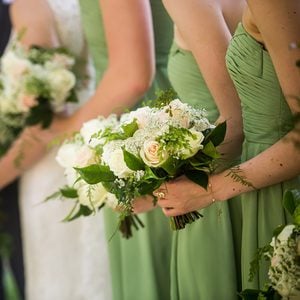 A candid photo of bride and her bridesmaids wearing light green bridesmaid dresses and holding a gorgeous bouquet. White and pink roses with baby