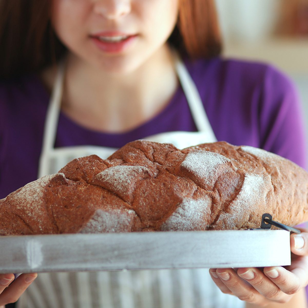 Young woman holding tasty fresh bread in her kitchen