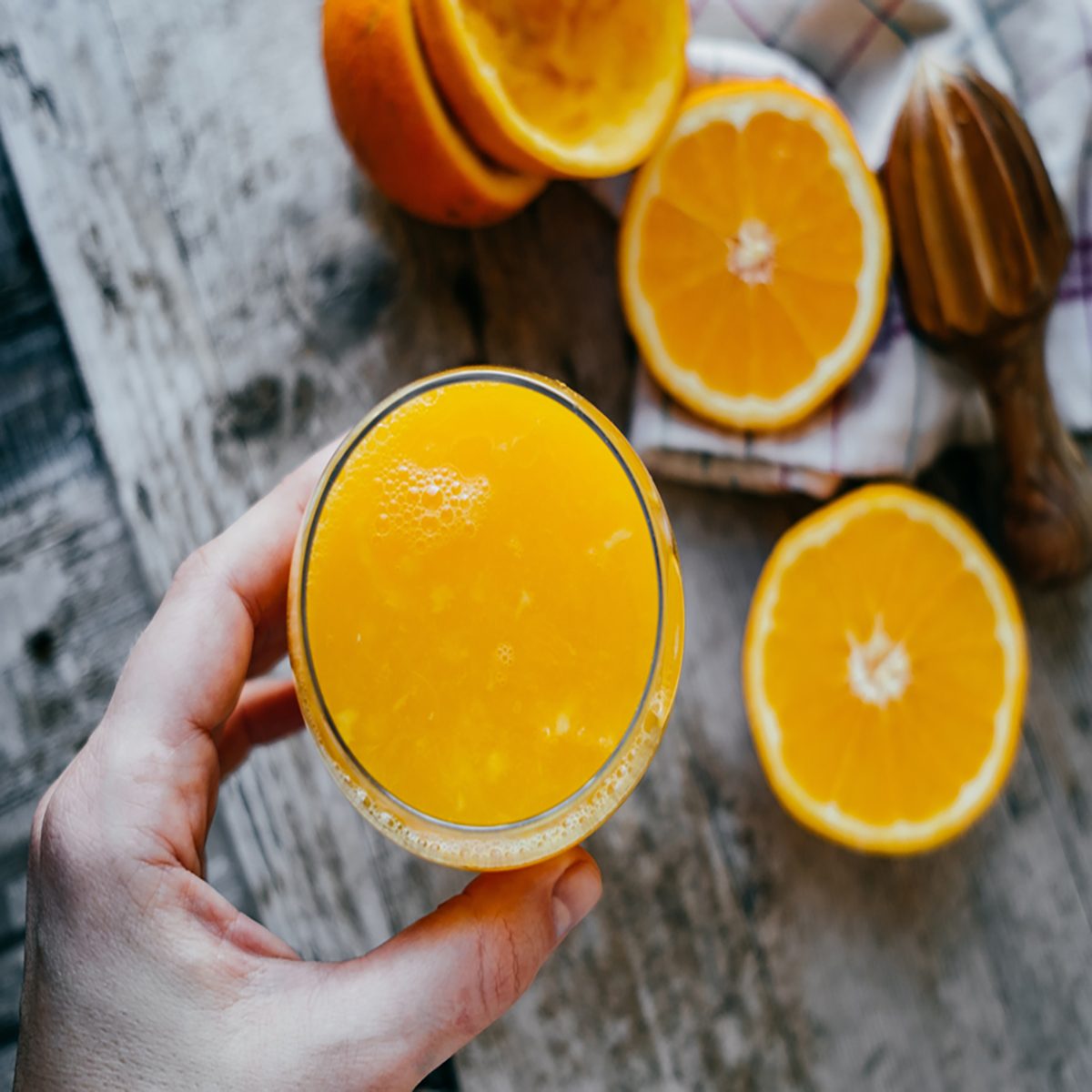 Woman Hand with juice glass and Oranges on wooden background.