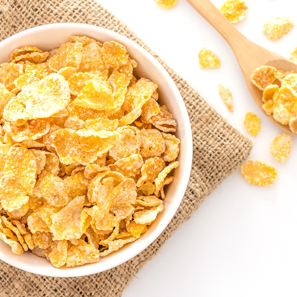 bowl of cornflakes and cornflakes on wooden spoon over a sackcloth on white table background, Top view with copy space; Shutterstock ID 492732964; Job (TFH, TOH, RD, BNB, CWM, CM): Taste of Home