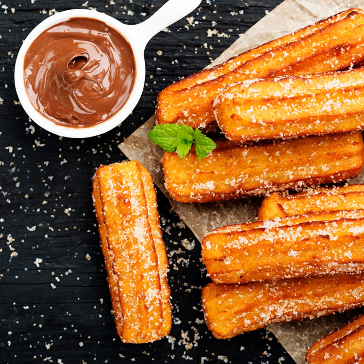 Churros with sugar and chocolate sauce on black background.