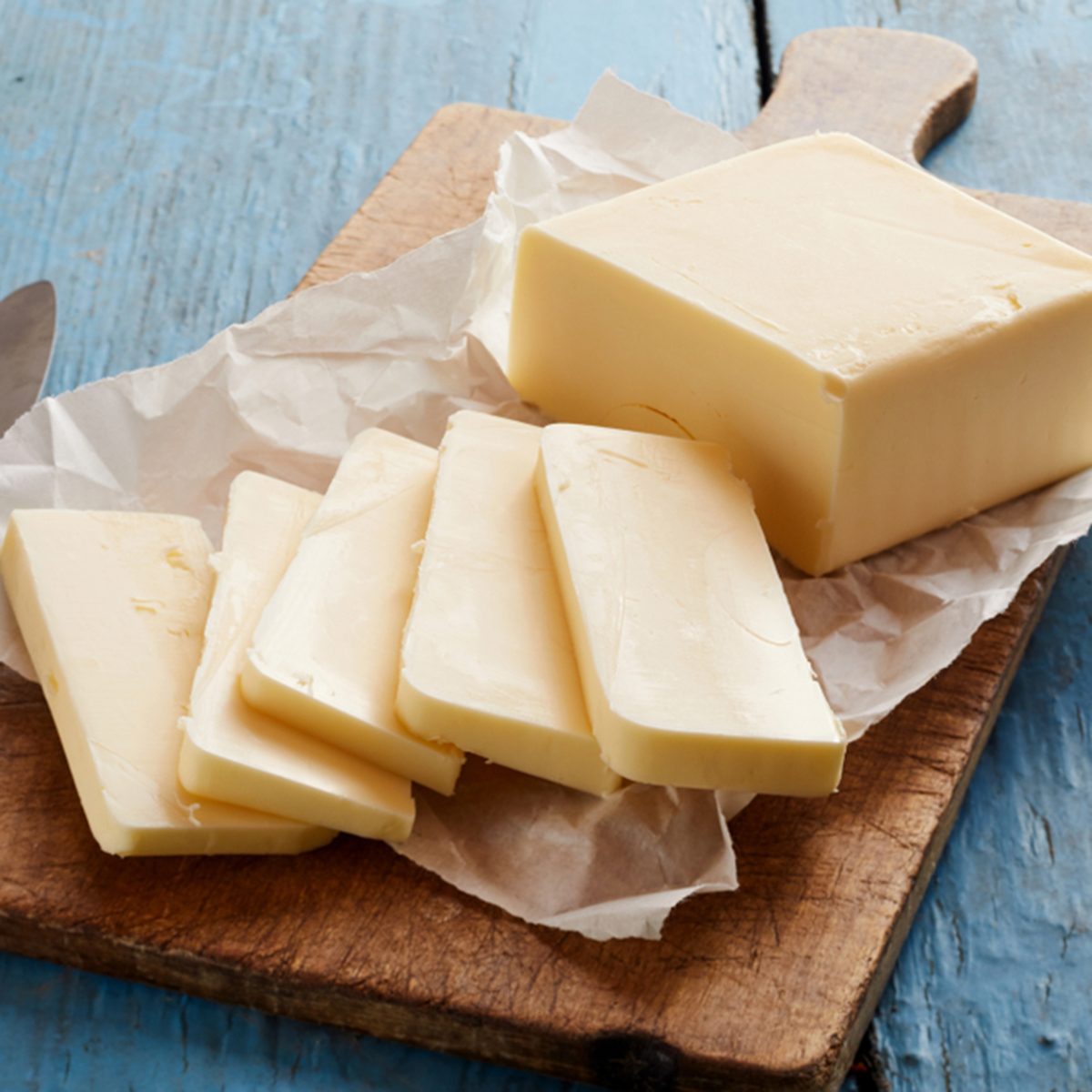 Block of butter sliced on cutting board against wooden background