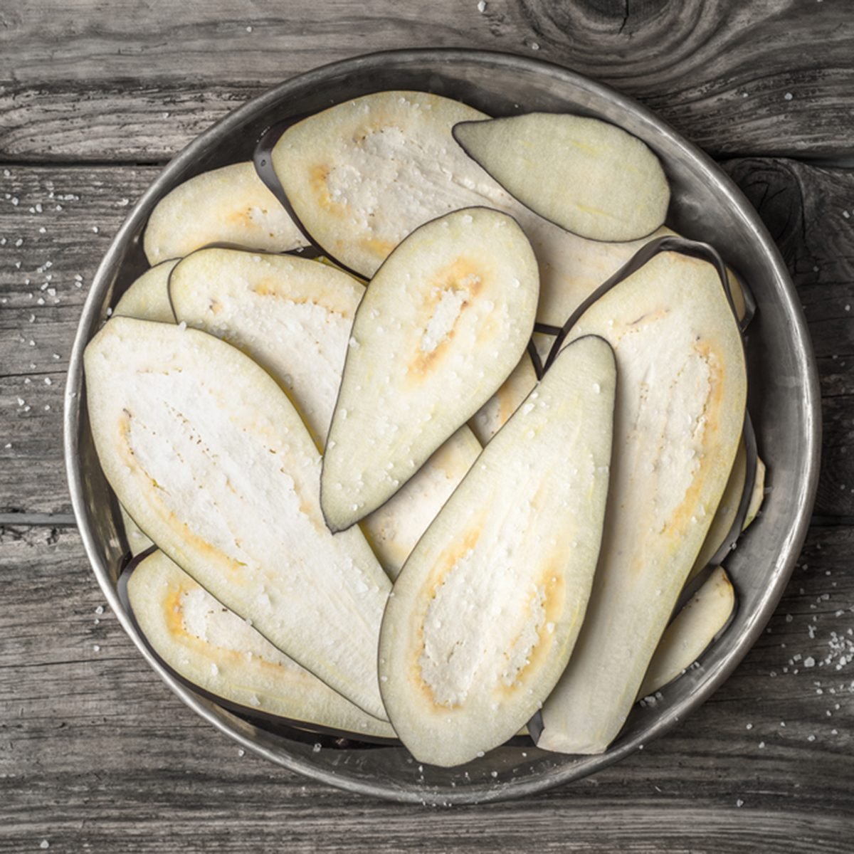 Sliced eggplants with salt in the metal plate on the wooden table top view