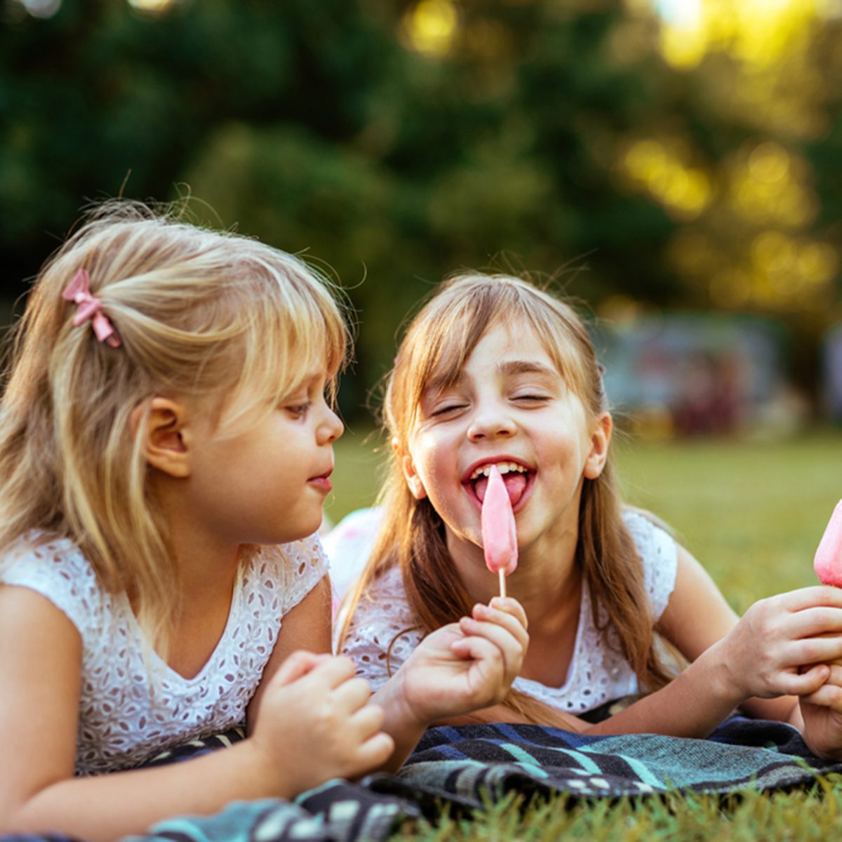 Close up portrait of two blonde girls eating ice cream on a picnic.