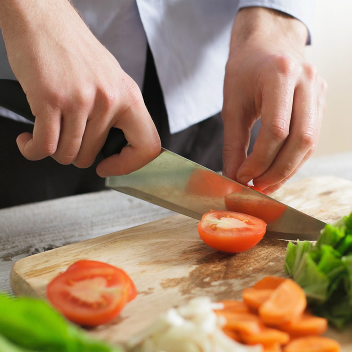 Close up of male hand cutting tomato on cutting board with sharp knife