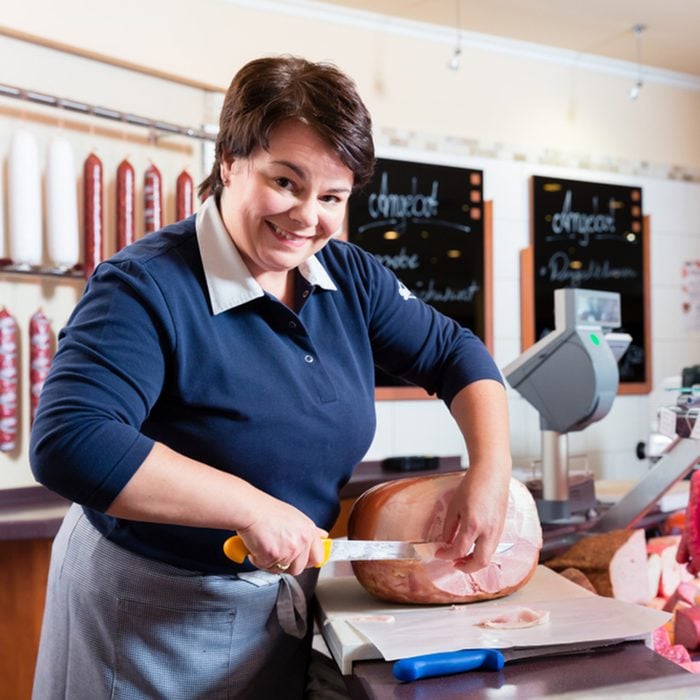 Experienced butcher shop assistant cutting ham to sell it