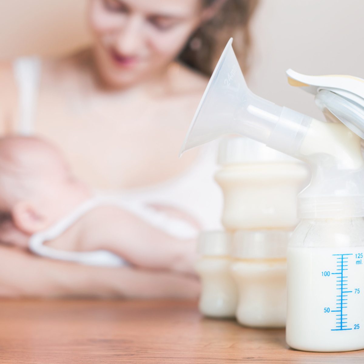 Manual breast pump and mother feeding at background