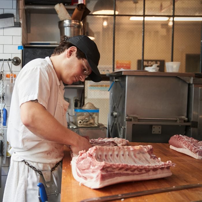 Young butcher cutting meat to sell at a butcher