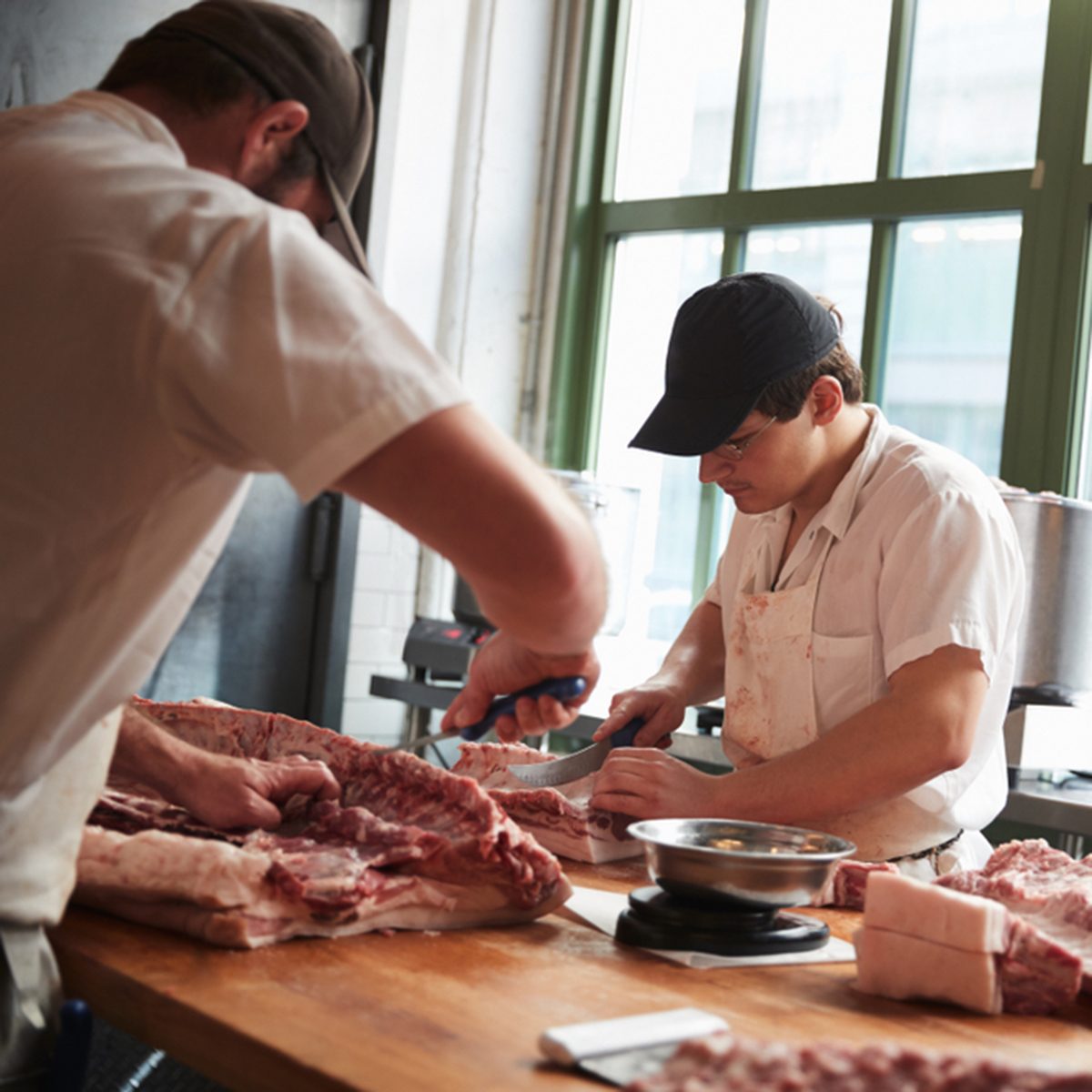 Two butchers cutting meat to sell at a butcher