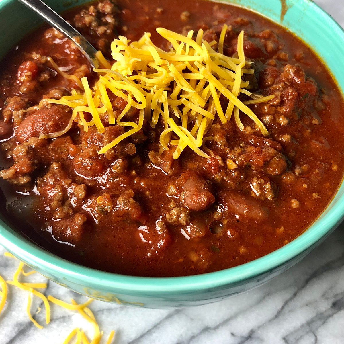 Homemade chili with cheese in a colorful bowl on white granite; Shutterstock ID 1282288555; Job (TFH, TOH, RD, BNB, CWM, CM): Taste of Home
