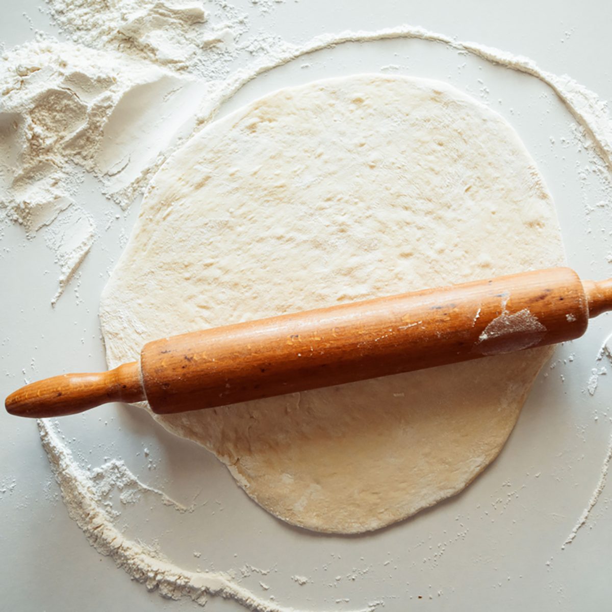 Block of freshly made pastry rolled out on a floured work surface with a wooden rolling pin