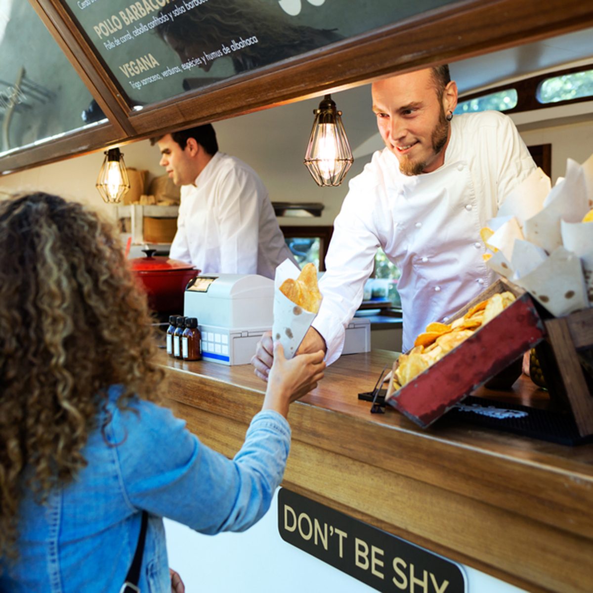 Portrait of beautiful young woman buying barbecue potatoes on a food truck in the park.