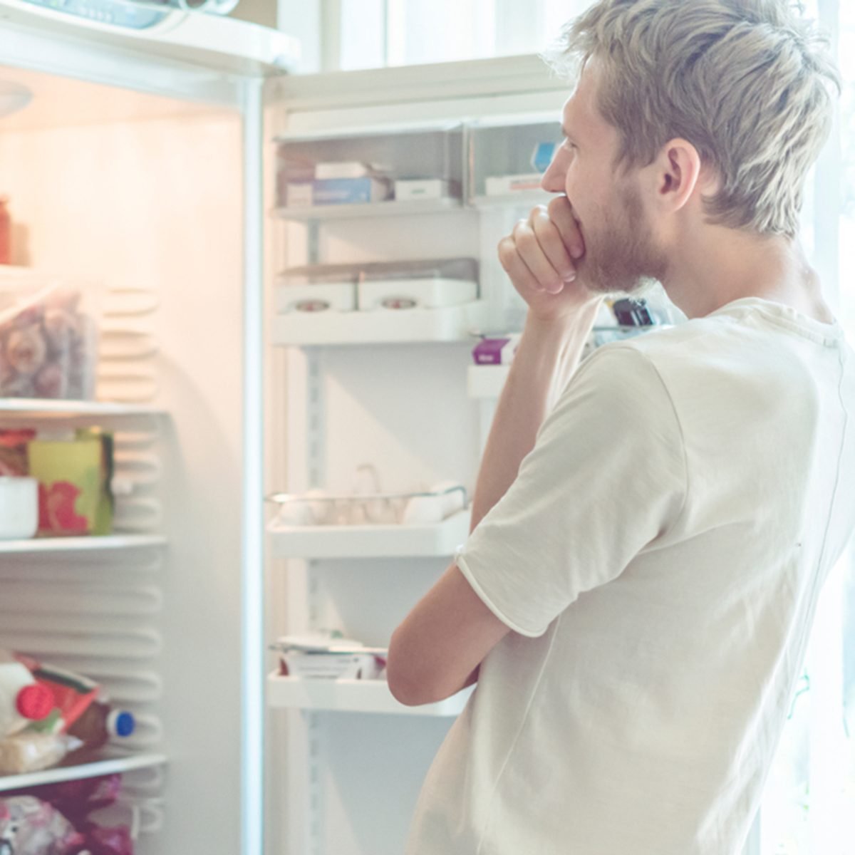 young man searching for food in fridge at home