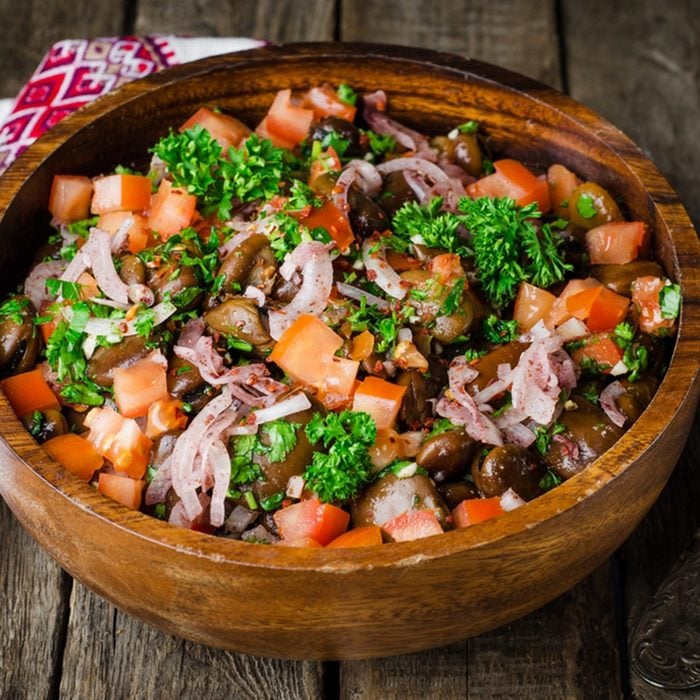 salad vith fava beans, tomatoes, onions and greens in wooden bowl