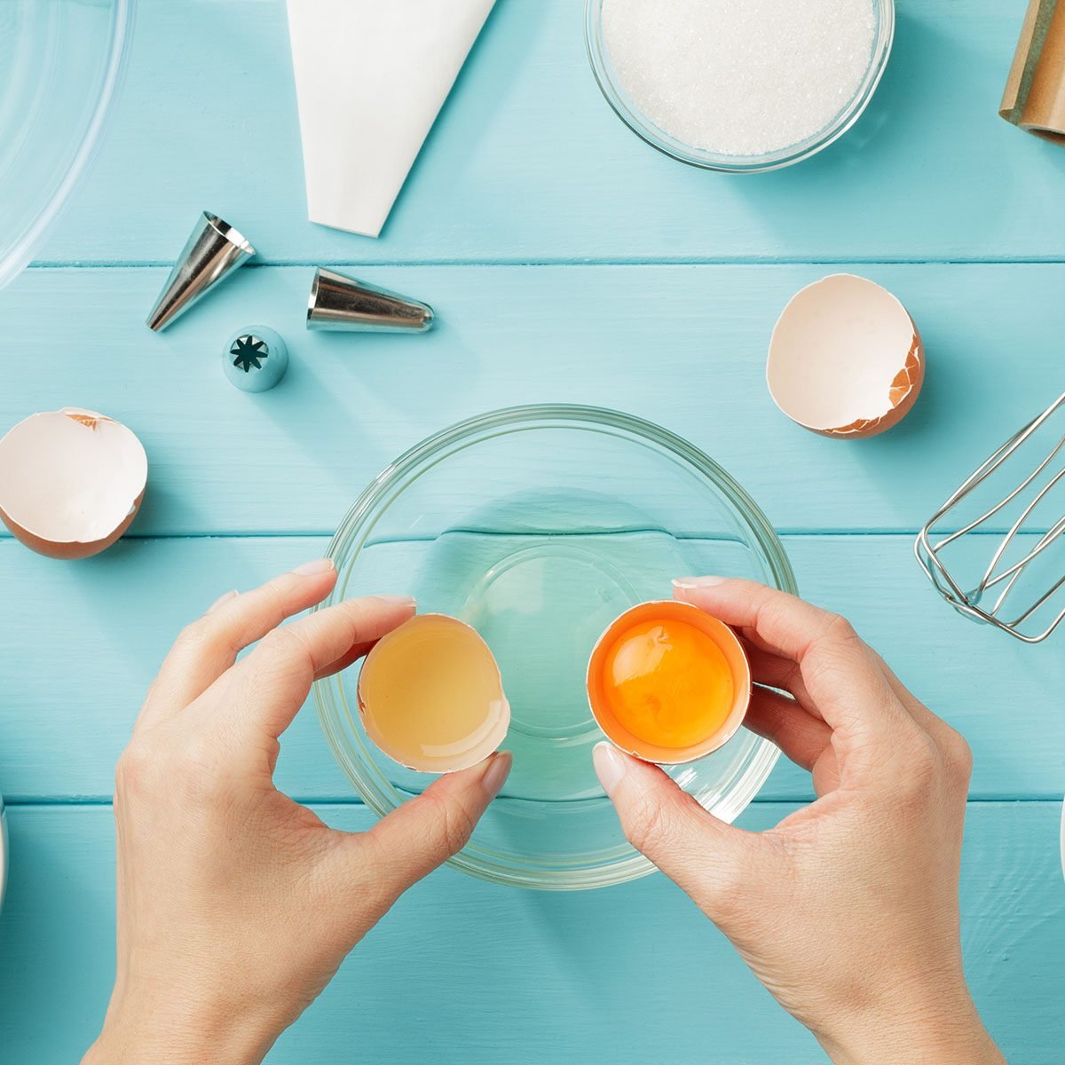 Female hands separate egg white from yolk for whipped cream. Step by step recipe of meringue with ingredients and utensils. Flat lay.; Shutterstock ID 1019679694; Job (TFH, TOH, RD, BNB, CWM, CM): -