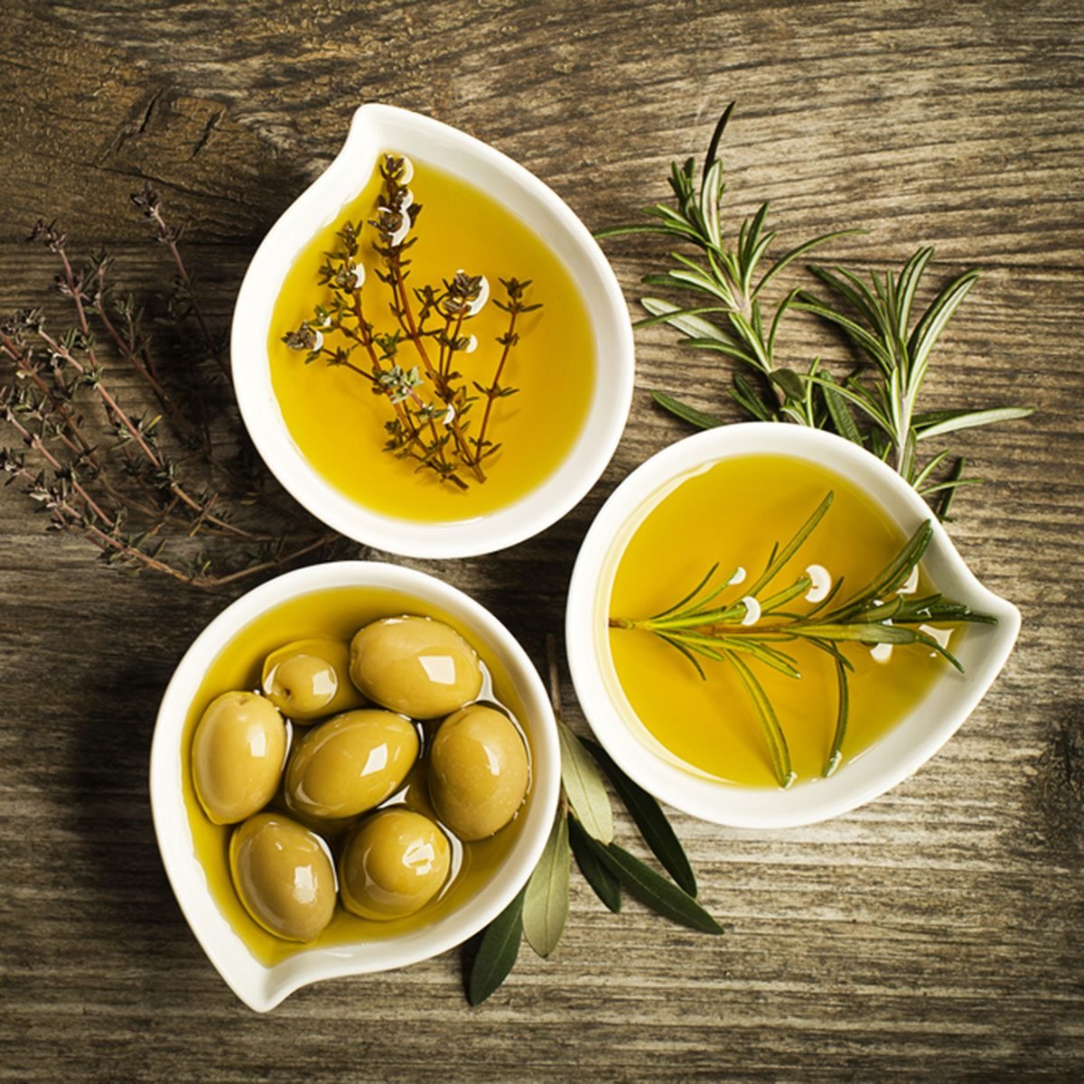 Olive oil with fresh herbs on wooden background.