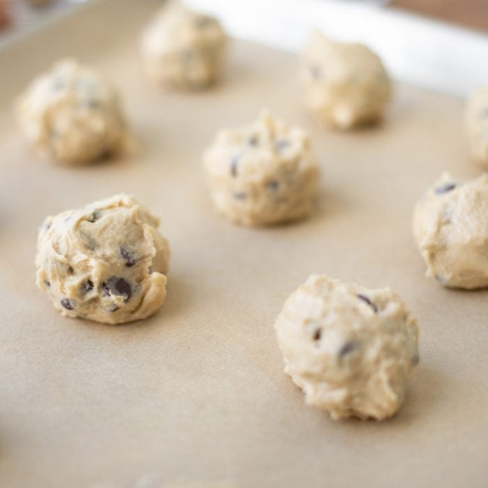 Close up on rows of chocolate chip cookie dough balls on a parchment paper lined baking sheet
