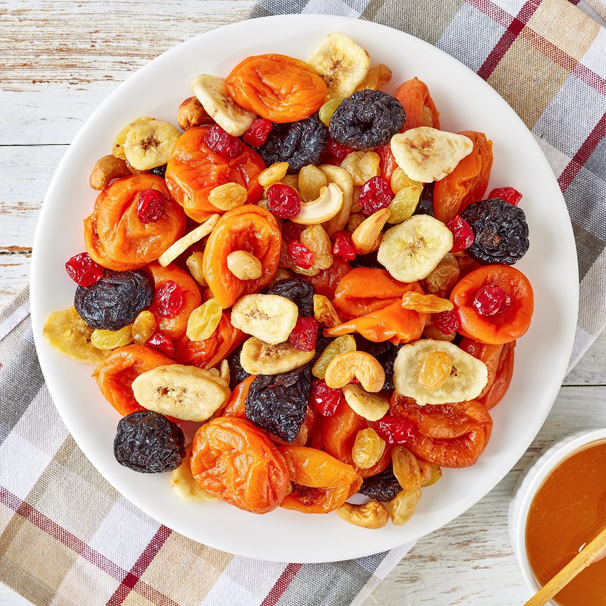 dried Fruits and Nut Mix bowl - banana slices, apricots, raisins, prunes, cherries and cashew on a rustic table with honey in a bowl, horizontal view from above, close-up, flatlay
