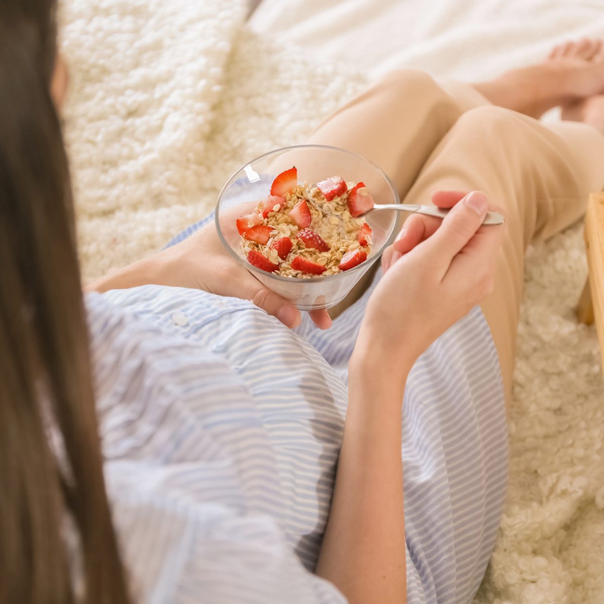 Pregnant woman with strawberry oatmeal porridge sitting on bed