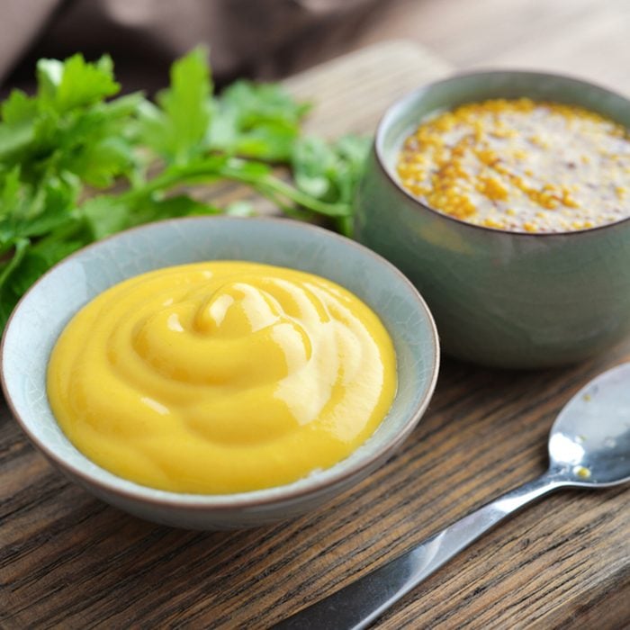 Mustard in the assortment: Dijon mustard and burning Russian mustard in bowls on wooden background