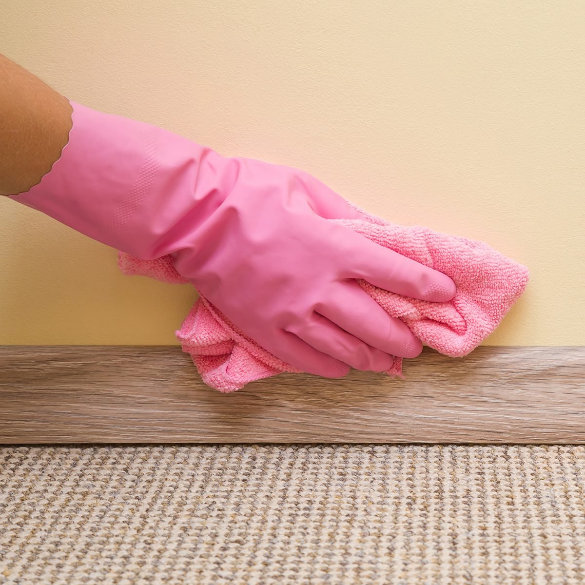 Hand in rubber protective glove with microfiber cloth cleaning baseboard on the floor from dust at the wall. Early spring cleaning or regular clean up. Maid cleans house.; Shutterstock ID 687988345