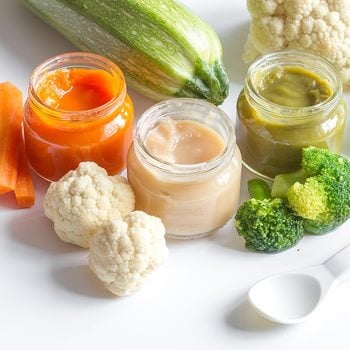 baby mashed with spoon in glass jar on white background
