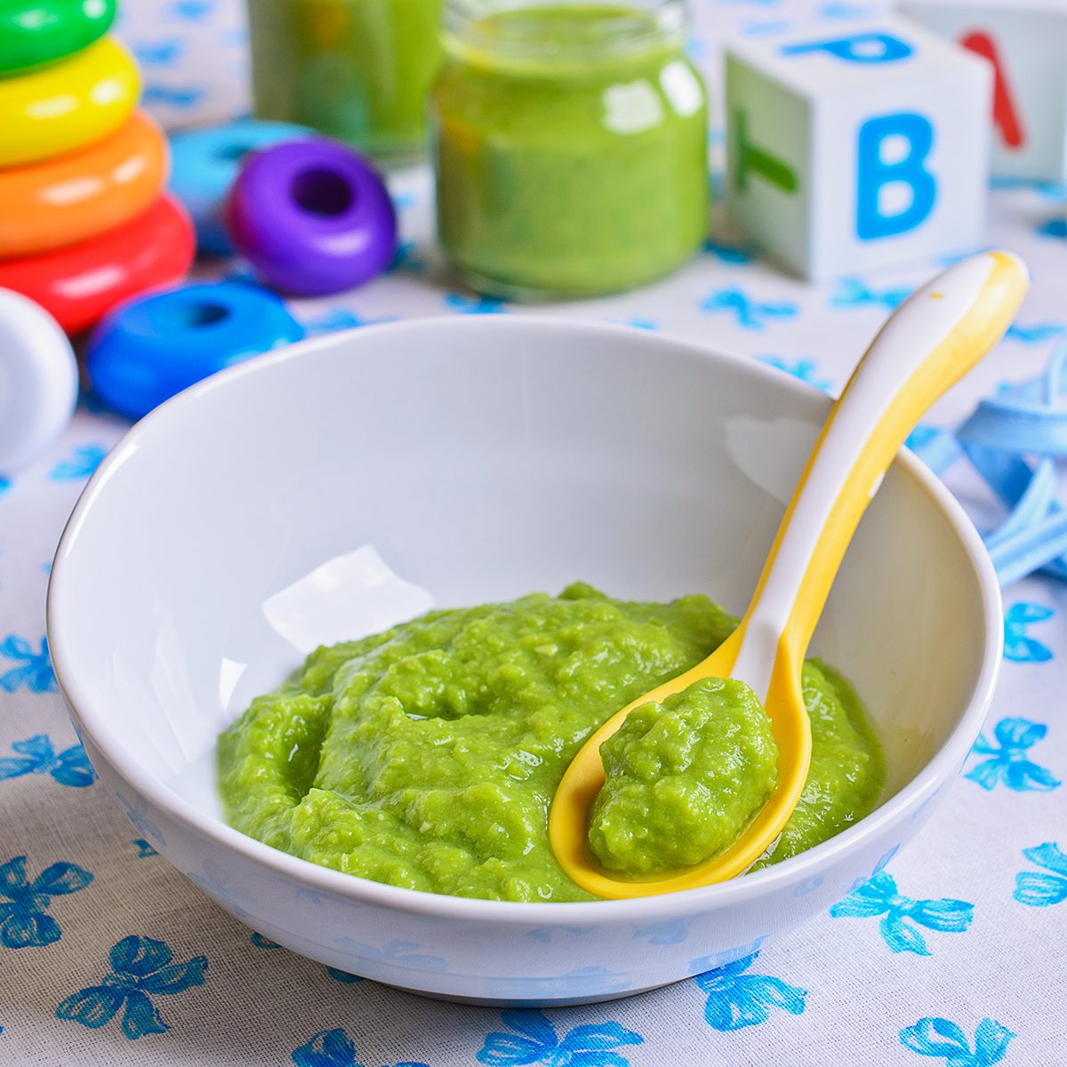 Puree of green in the small bowl is on the background of childrens toys