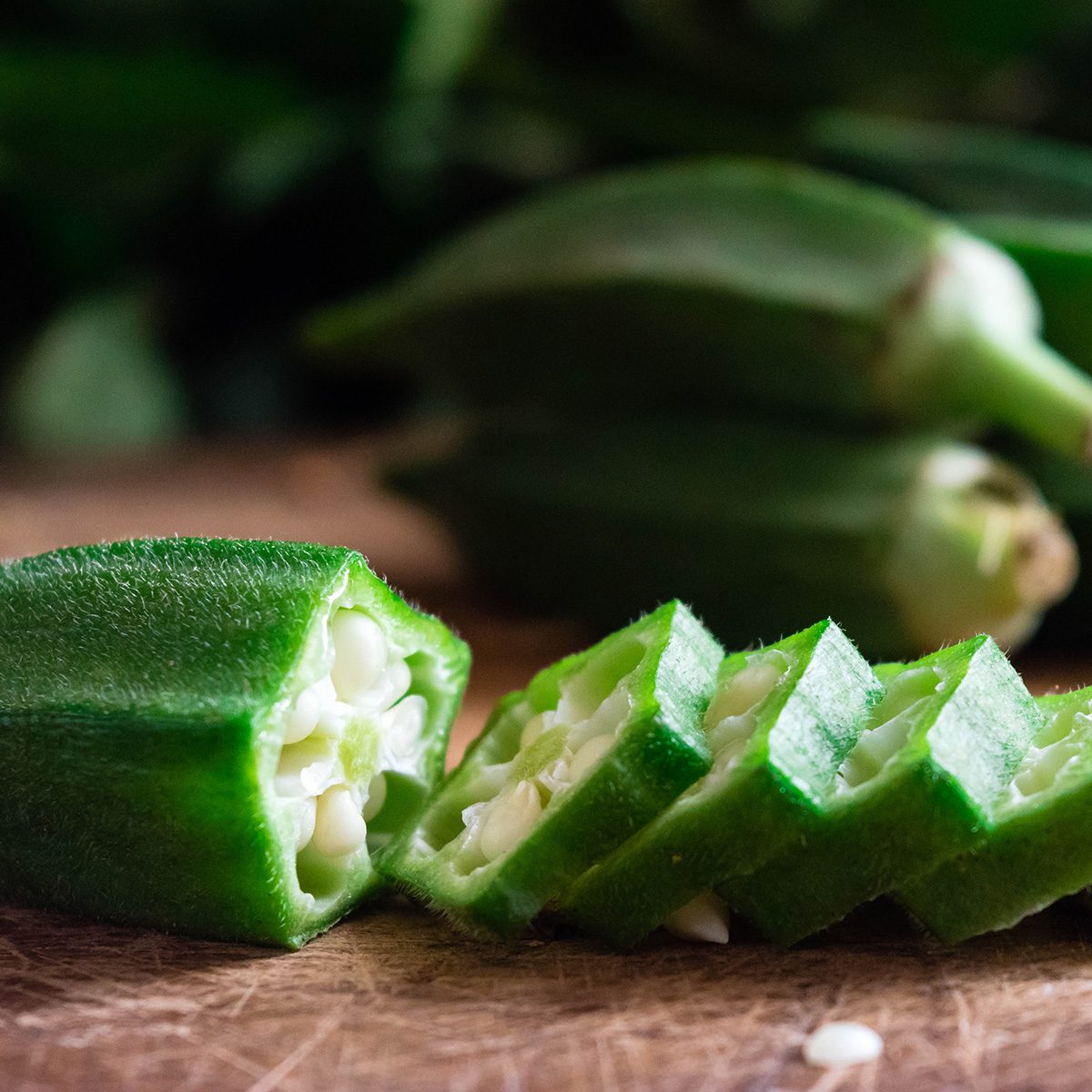 Close up of Farm fresh raw okra slices on wooden rustic aged chopping board.