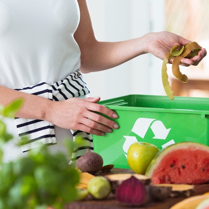 Woman recycling organic kitchen waste by composting in green container during preparation of meal