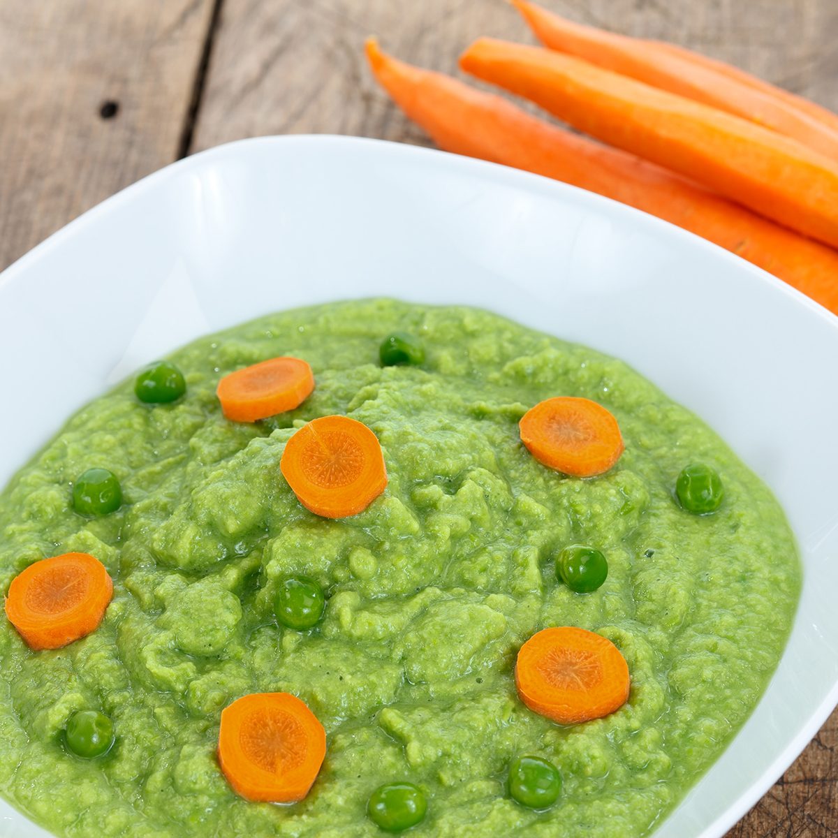 Baby food with green peas and carrots on wooden table