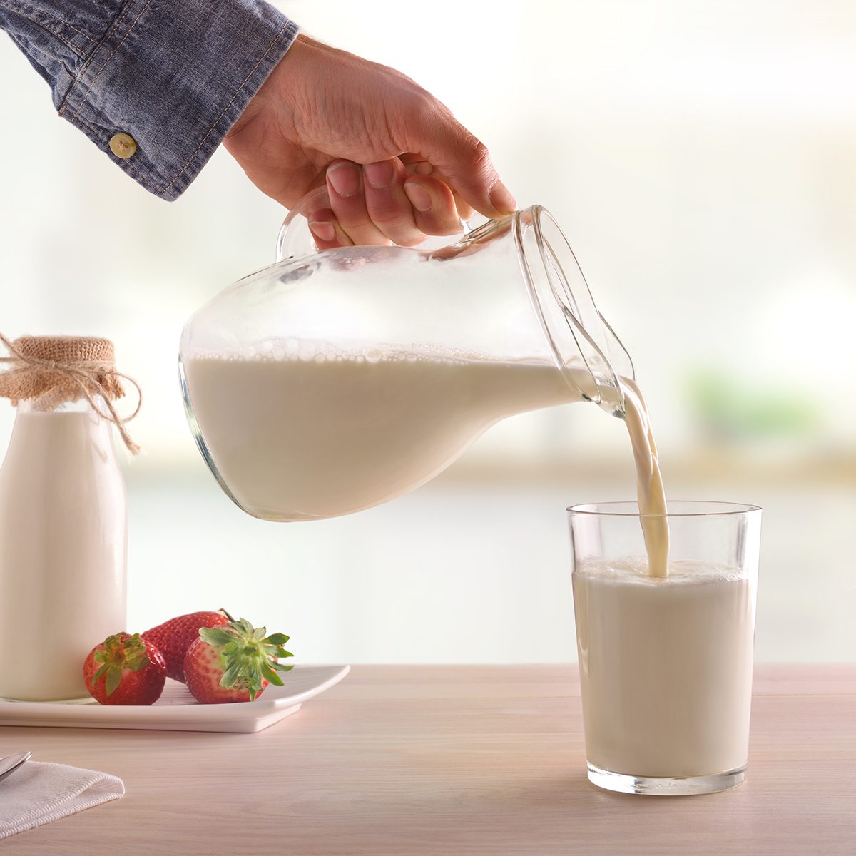 Serving breakfast milk with a jug in a glass on a white wooden kitchen table.