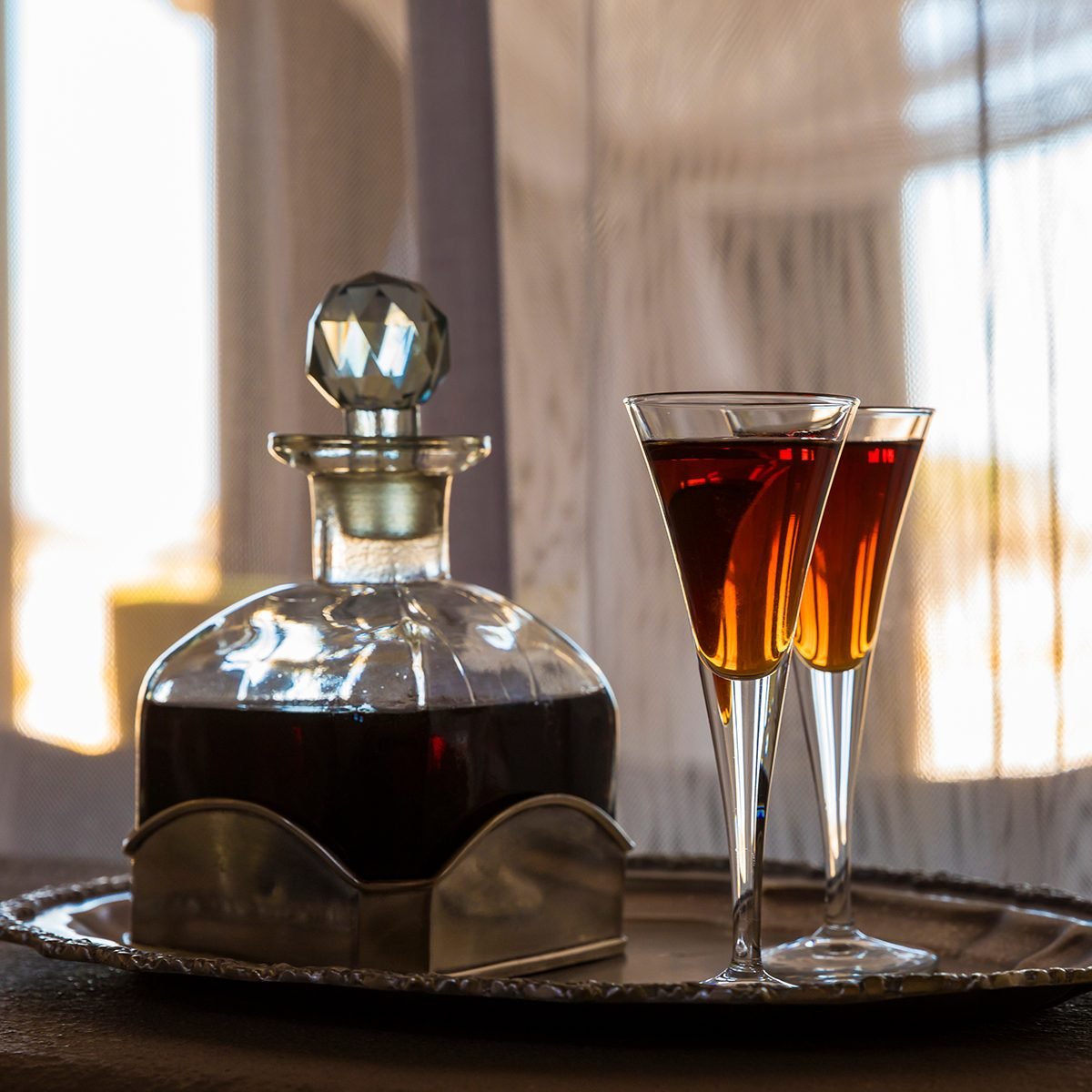 Two glasses an a carafe filled with red sherry in a room with a lot of sun