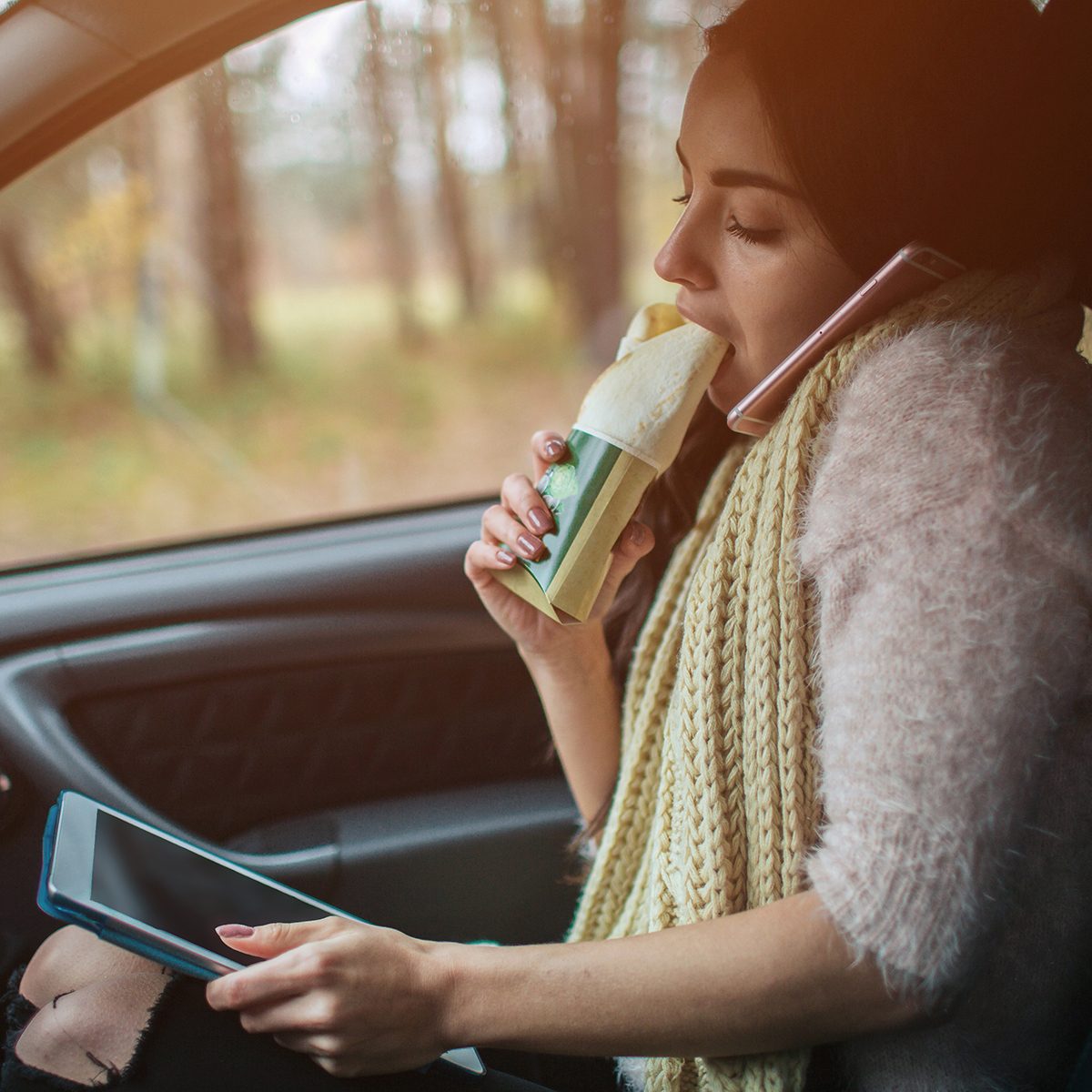 Busy woman is in a hurry, she does not have time, she is going to eat snack on the go. Worker eating and talking on the phone at the same time.