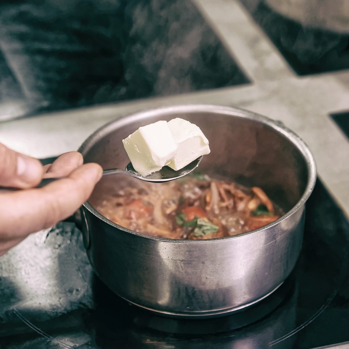 Chef is adding pieces of butter to a dish cooking on electric induction plate